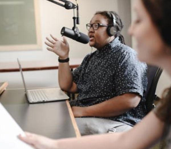 University of Akron student speaks into a microphone while recording audio in a campus radio studio.