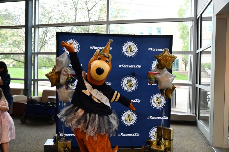 A person in a kangaroo mascot costume poses in front of a backdrop with 