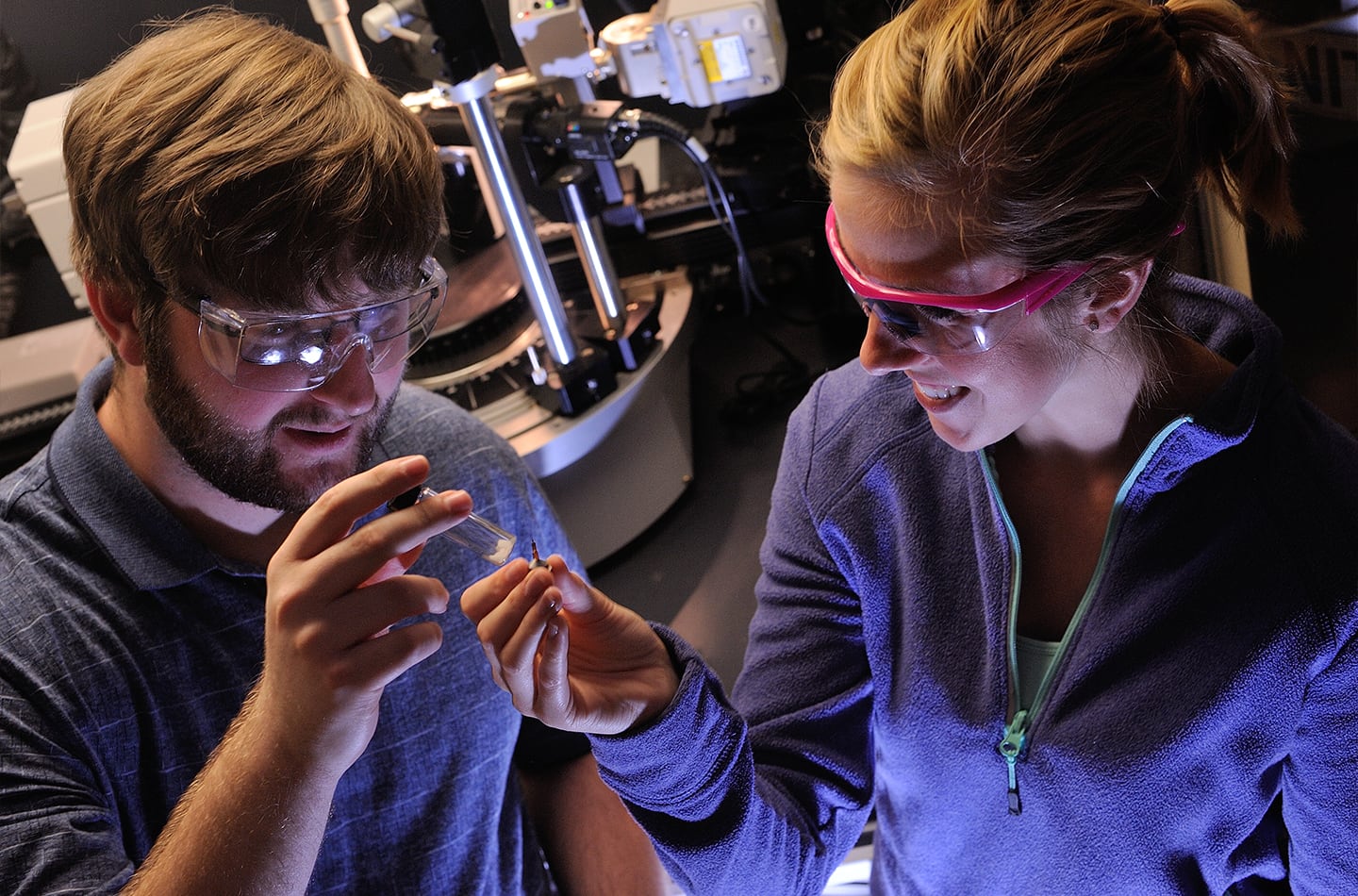 Caucasian young man with brown hair and beard and young woman with blonde hair looking in test tubes