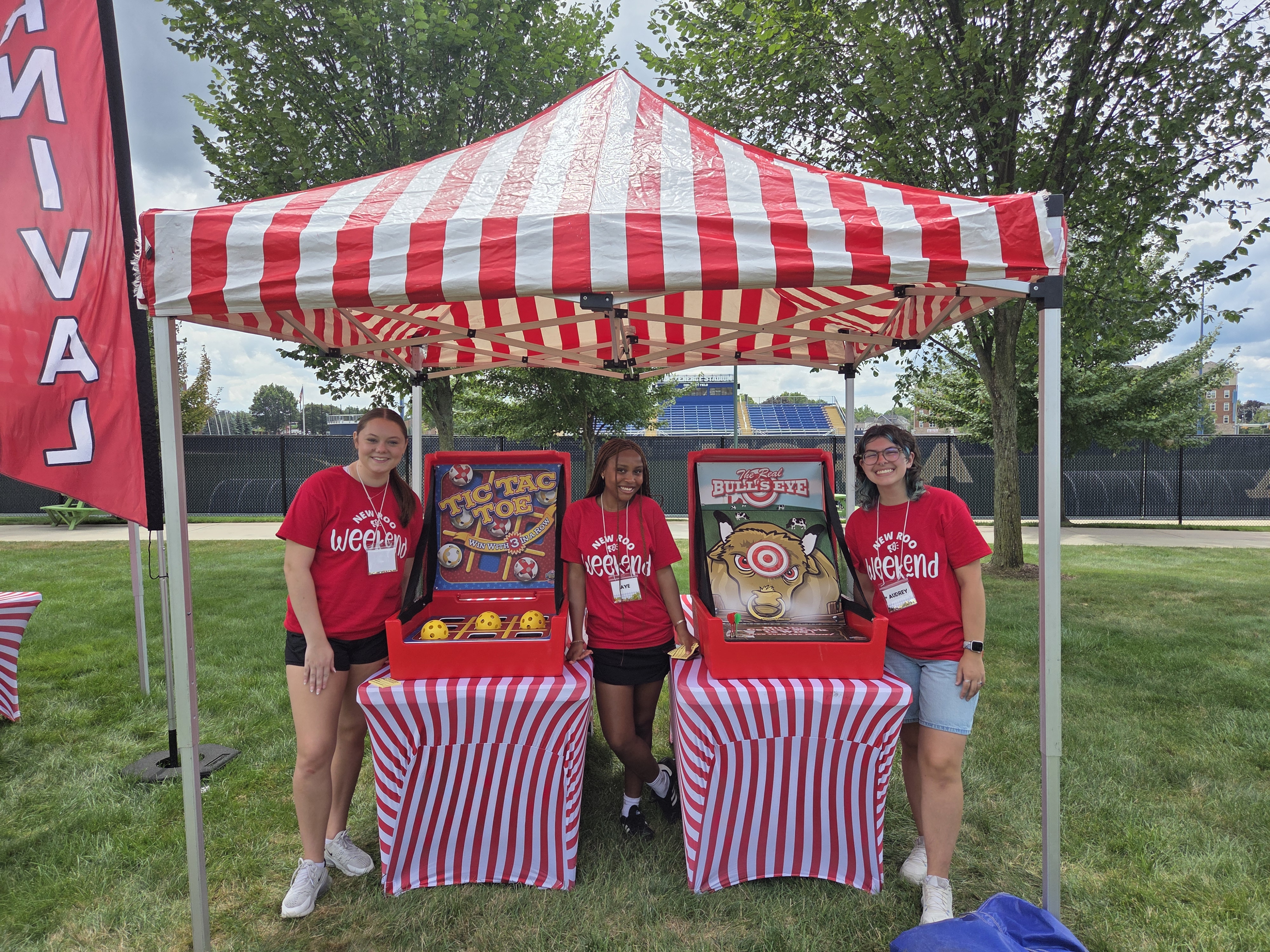 Three students standing with carnival games under a pop-up tent