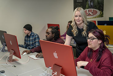 University of Akron instructor assists students working on Apple computers in a digital media classroom.