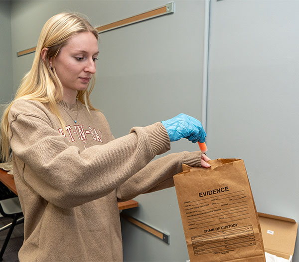 University of Akron student wearing gloves places a sample into an evidence bag during a forensic science lab exercise.