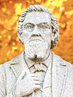 Statue of founder John R. Bucthel in front of tree with bright autumn leaves.