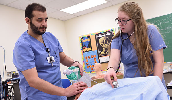 Two healthcare professionals in a clinical setting, with medical equipment visible in the background.