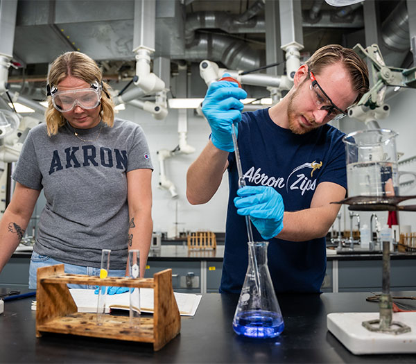 University of Akron chemistry students conduct a laboratory experiment, measuring and mixing liquids while wearing safety goggles and gloves.