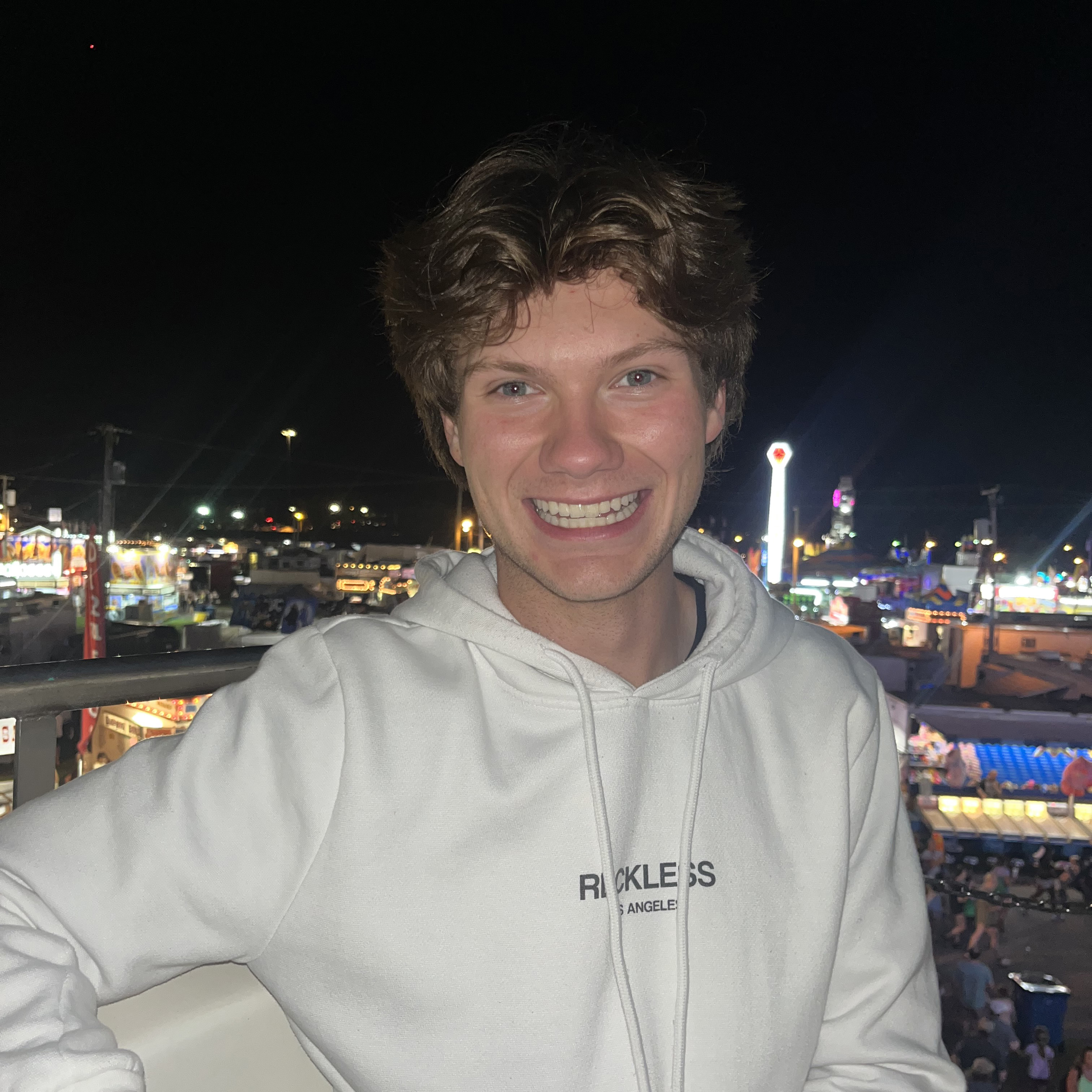 UAkron Online student AJ Stewart smiles at the camera in a white hoodies with a night scene in the background