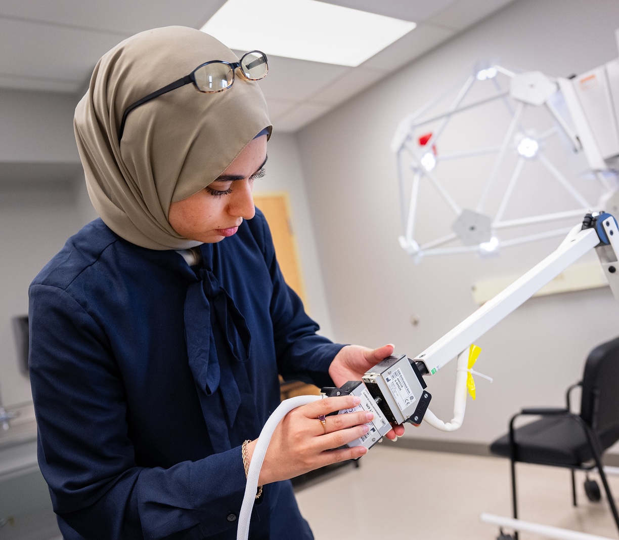 A woman in a hijab adjusts a piece of laboratory equipment in a modern lab setting.