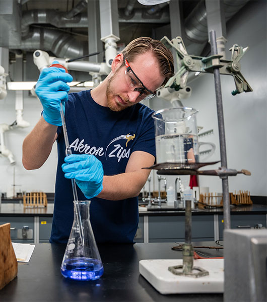 Akron student pipetting liquid into a beaker in a chemistry lab