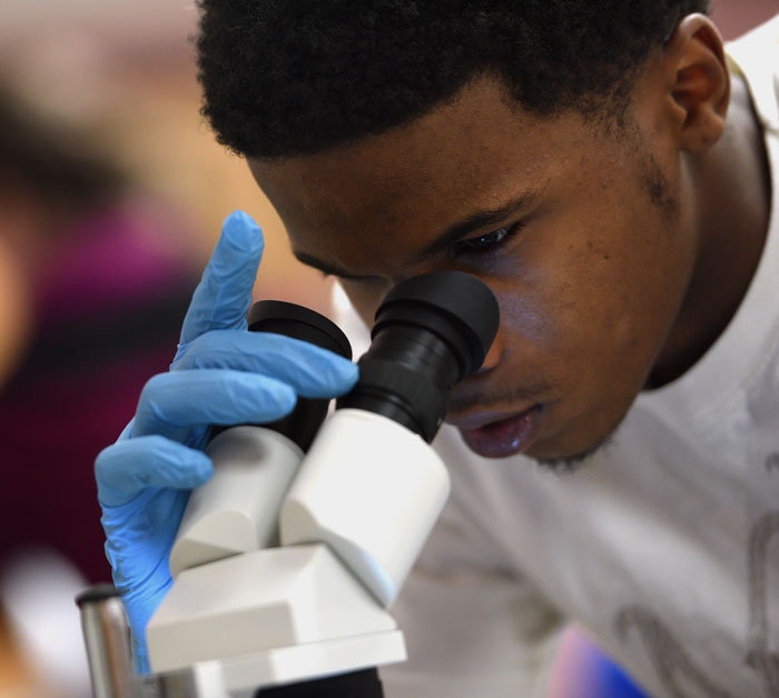 University of Akron student wearing gloves looks through a microscope during a crime lab exercise.
