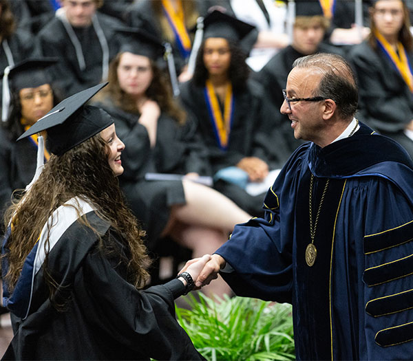 University of Akron graduate shakes hands with the university president while crossing the commencement stage during graduation.