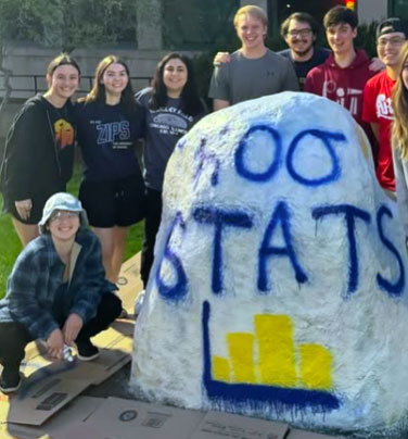 University of Akron statistics students pose beside a painted campus rock that reads “Roo Stats.”