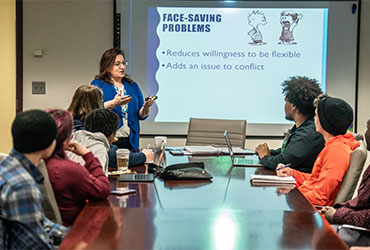students participate in a classroom discussion while a faculty member presents communication concepts.