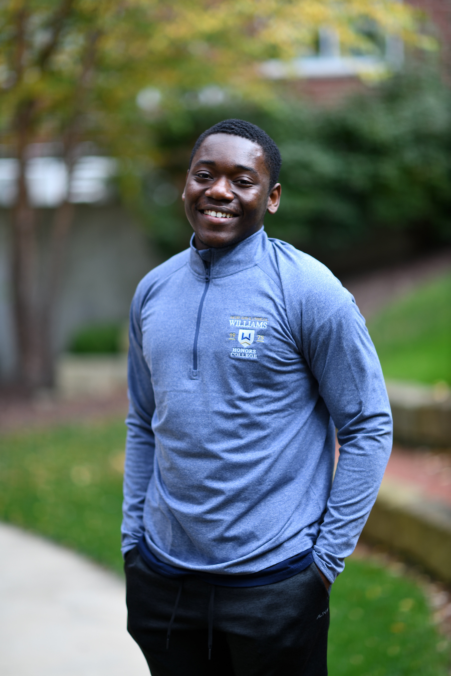 Young man wearing light blue fleece standing in front of greenery.