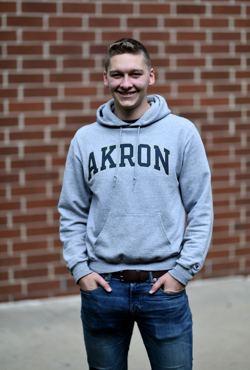 Photo of man in gray hoodie against red bricj background.