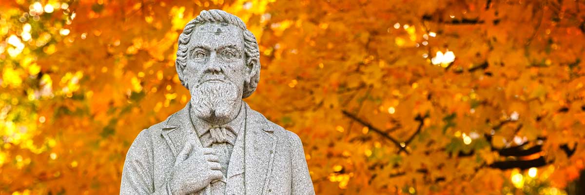 A statue of the University's founder with yellow leaves behind him